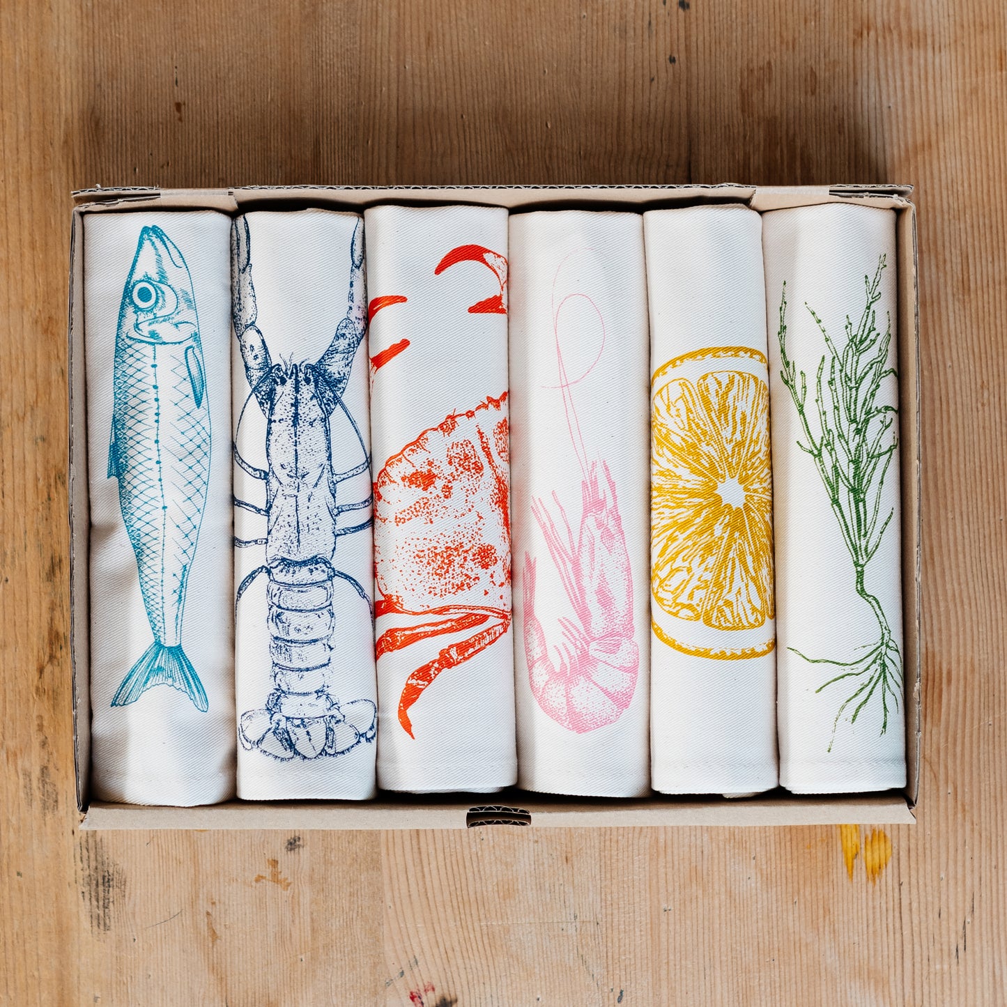 Seafood napkin gift set by Lottie Day featuring handprinted crab, blue lobster, prawn, mackerel, samphire and lemon illustrations on cotton napkins